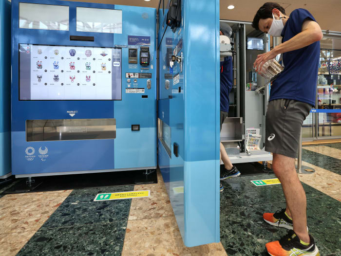 A customer buys an item from a vending machine at the Tokyo Olympics.